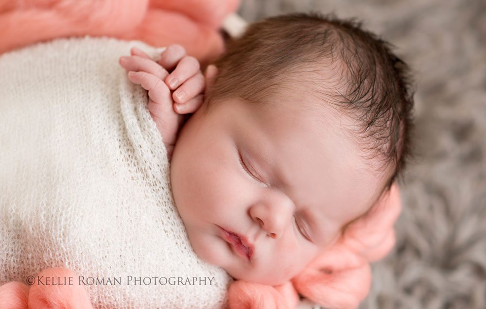 Milwaukee Newborn Photos baby girl close up of face and hands sleeping in a white swaddle wrap in a bucket filled with coral fluff on top of grey rug