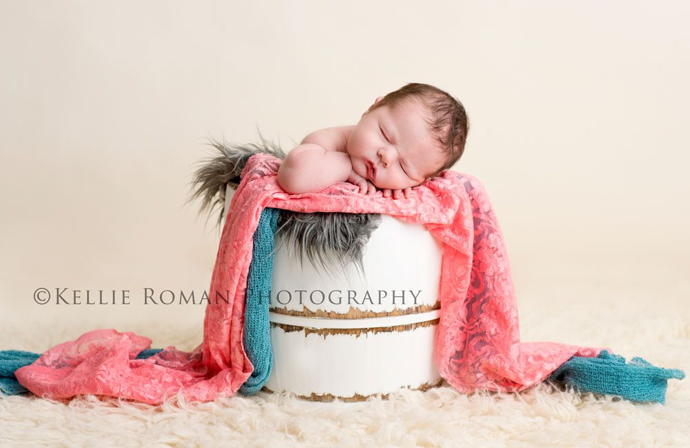 Milwaukee Newborn Photos newborn girl in white bucket in front of ivory backdrop bucket layered with coral teal and grey fabric and onto of ivory rug 