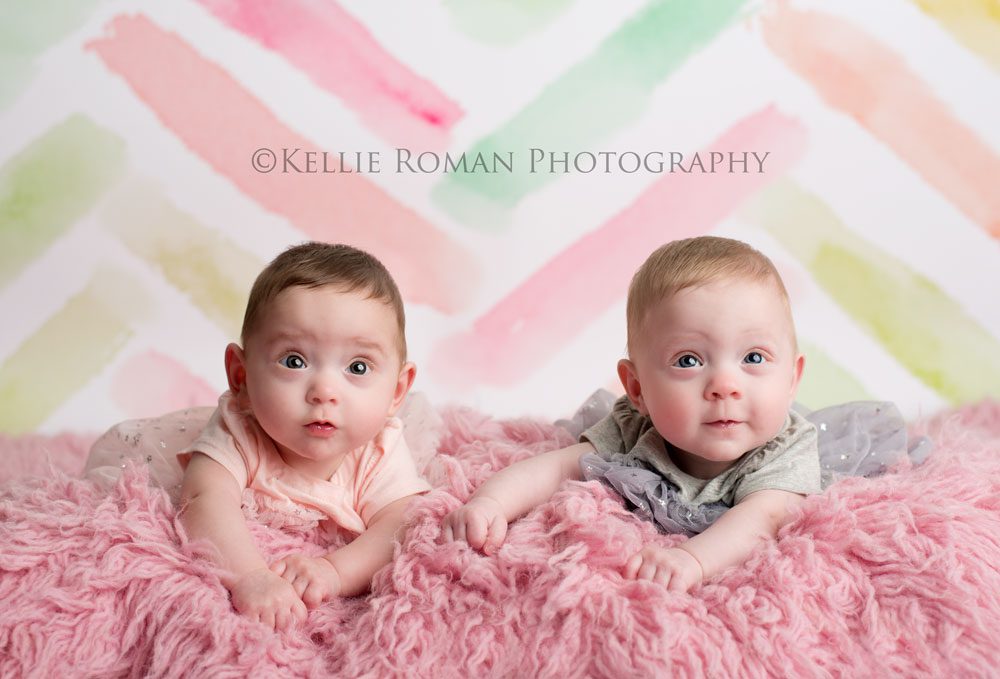Milwaukee Twin Photographer six month old girl twins laying on belly on top of pink rug infant of pastel pink green yellow backdrop