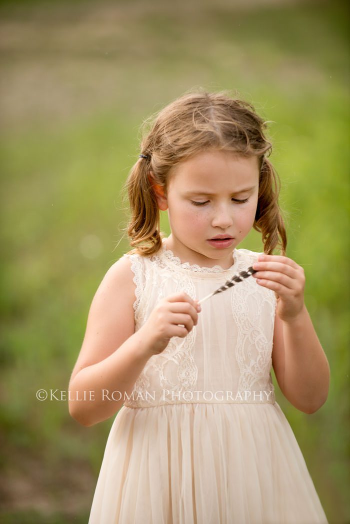 vintage style photo shoot young girl wearing ivory dress outside looking down at brown feather