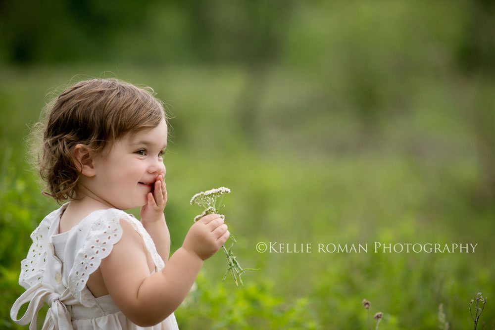 vintage style photo shoot baby girl holding white flower while smiling and cover her lips with her hand