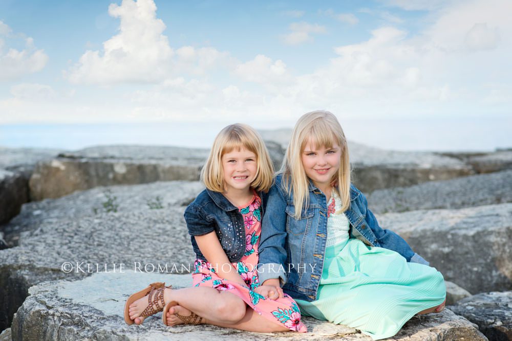 golden summer sisters sitting on big rocks with blue sky and clouds