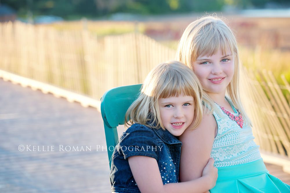 golden summer photo of sisters outside on chair on a boardwalk