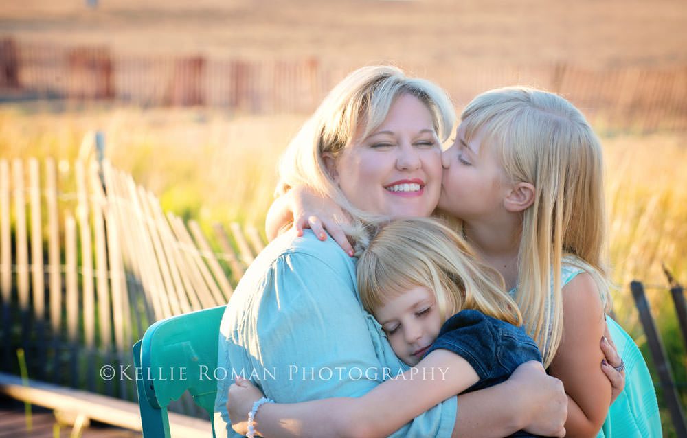 golden summer candid image of daughters kissing mom and cheek outside