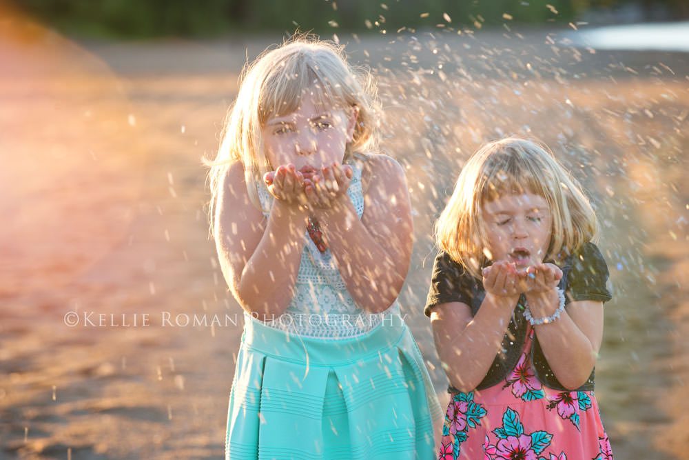 golden summer two girls on the beach blowing glitter that is sparkling in the sun