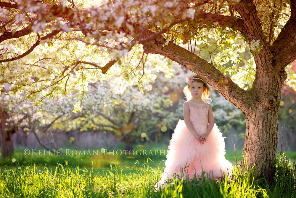 in full bloom girl in pink tule dress standing under crabapple tree in green grass