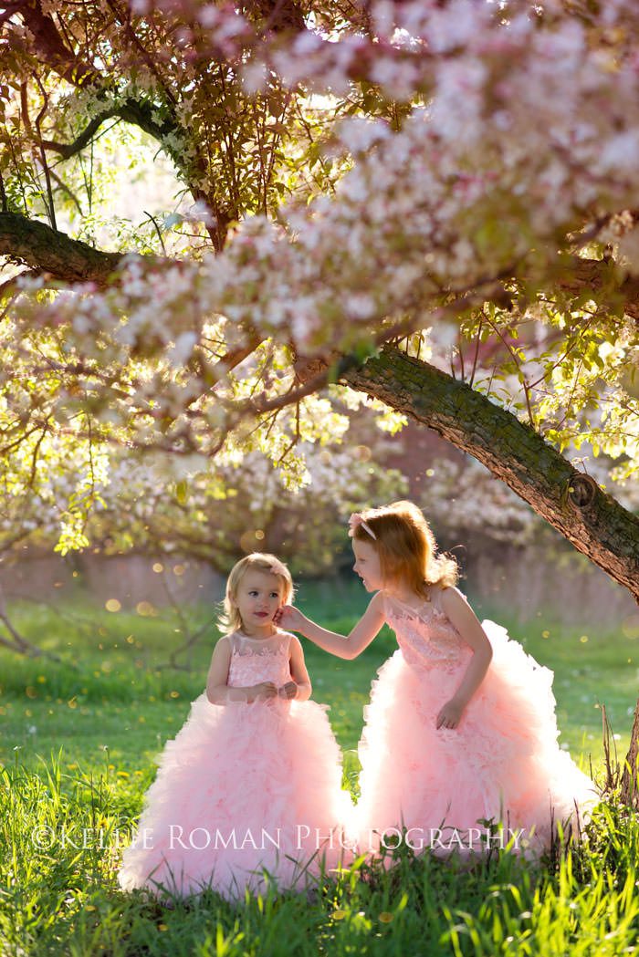 in full bloom sisters in big pink dresses standing outside under flowering tree