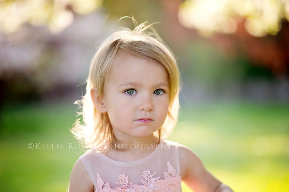 in full bloom little girl with blond hair standing outside with sunlight behind her