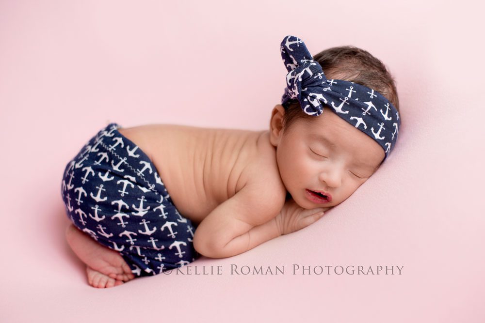little sailor girl newborn girl posed on top of pink fabric with navy pants and headband on with white anchors