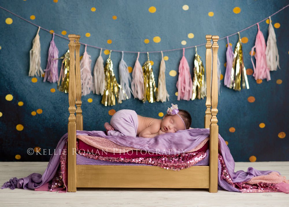 little sailor girl newborn girl sleeping on gold bed with navy gold and purple backdrop