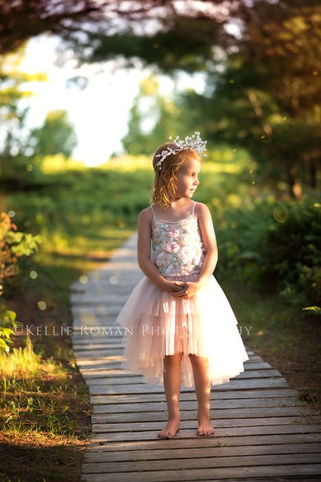 the great lakes girl standing in park on boardwalk in sunlight wearing pink dress 