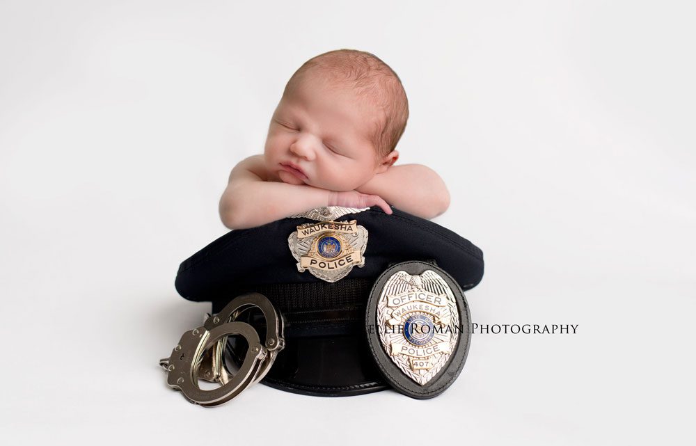 three big sisters baby boy posed on top of black police hat with badge and hand cuffs
