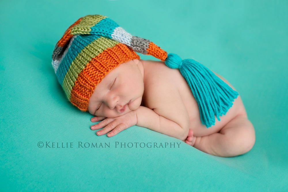three big sisters baby posed on aqua blanket with colorful striped tassel hat on