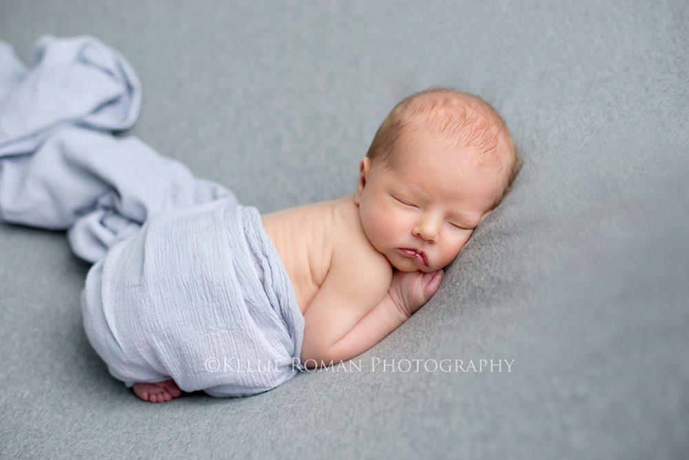super hero sleeping newborn boy posed on stomach onto of great blanket with grey wrap