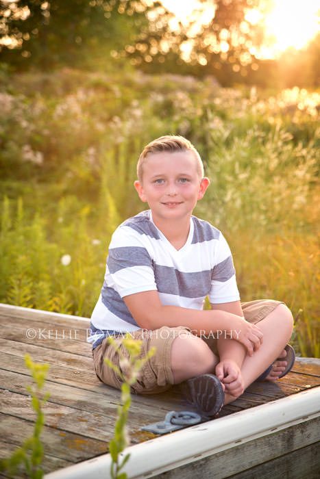 mother and son session boy sitting on old wood pier in a field with sun setting behind him
