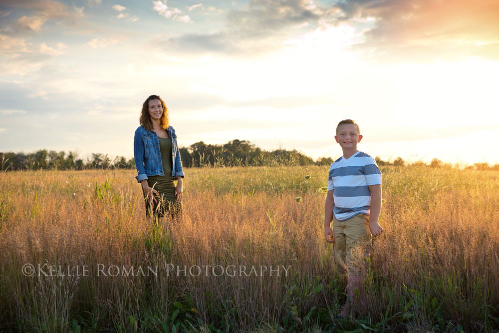 mother and son session mom and son standing in field of tall grass with sunlight and clouds behind them
