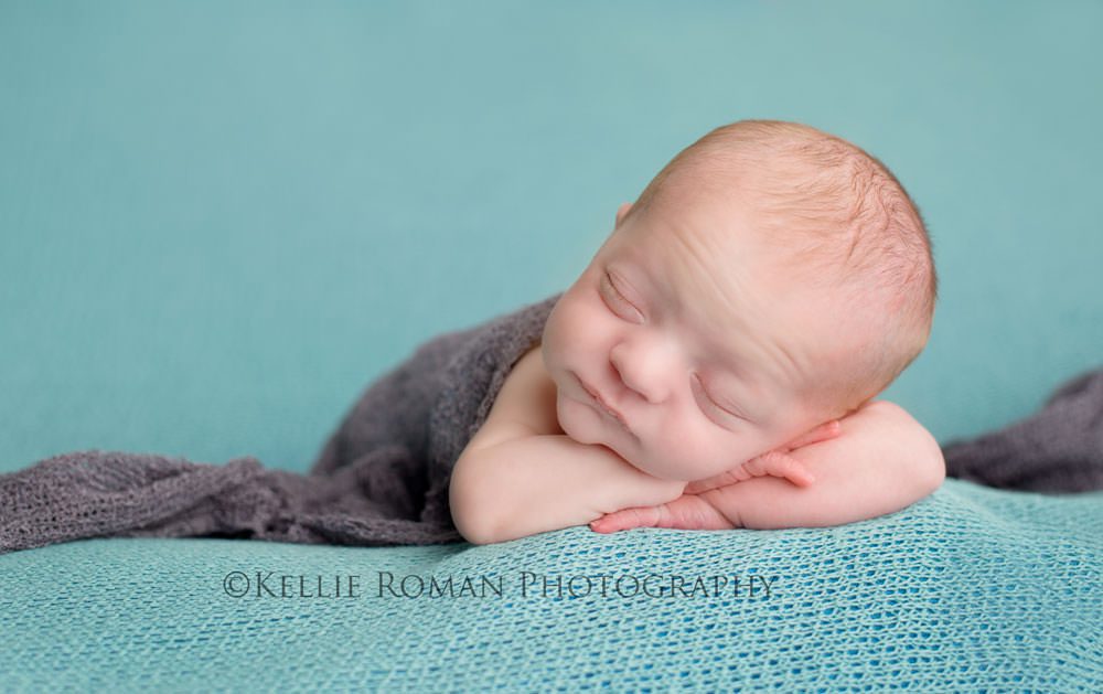 newborn photography newborn boy laying on tummy with his chin onto of his arms onto of a blue blanket with a grey wrap over him