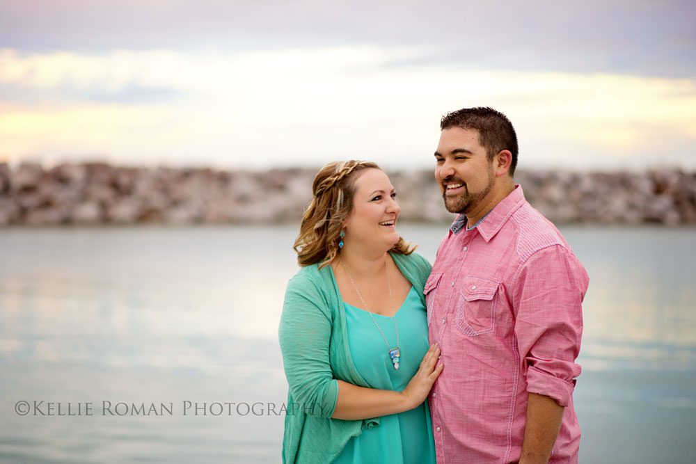 family photography couple standing in front of water smiling at each other wife wearing green shirt and husband wearing pink shirt