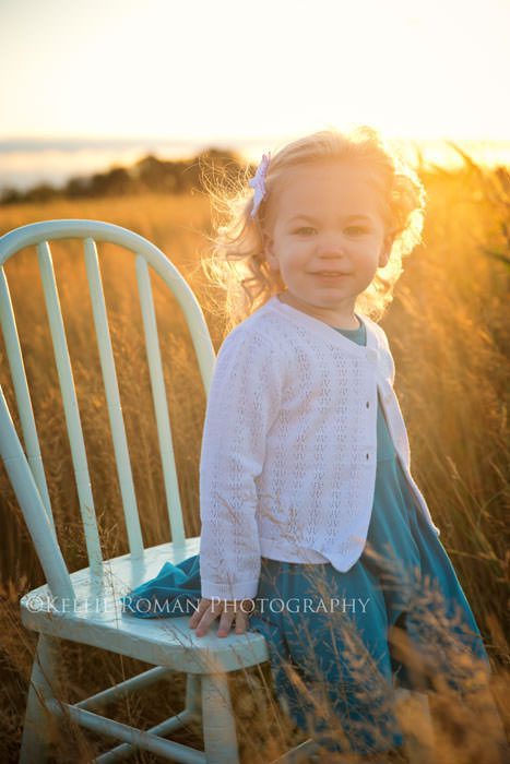 family photos toddler girl sitting on chair in a field of tall grass with sunlight shining from behind her