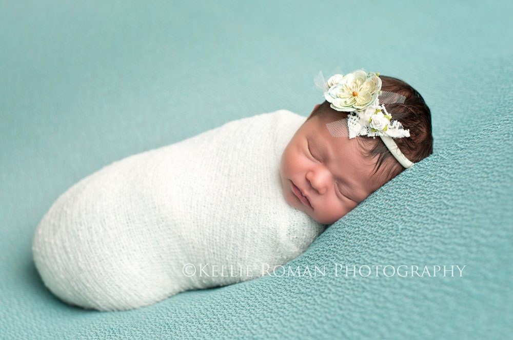 newborn session with baby girl wrapped in white swaddle onto of blue blanket with headband