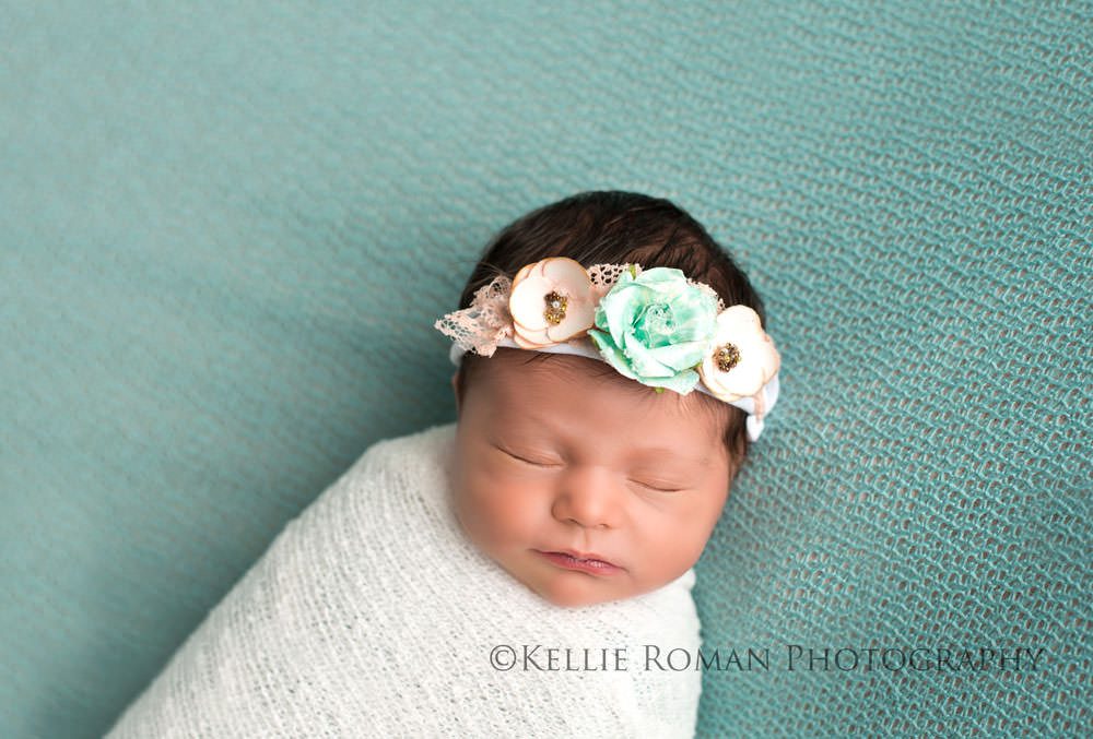 newborn session with baby girl wrapped in white swaddle blanket onto of a blue blanket with a blue and pink headband on