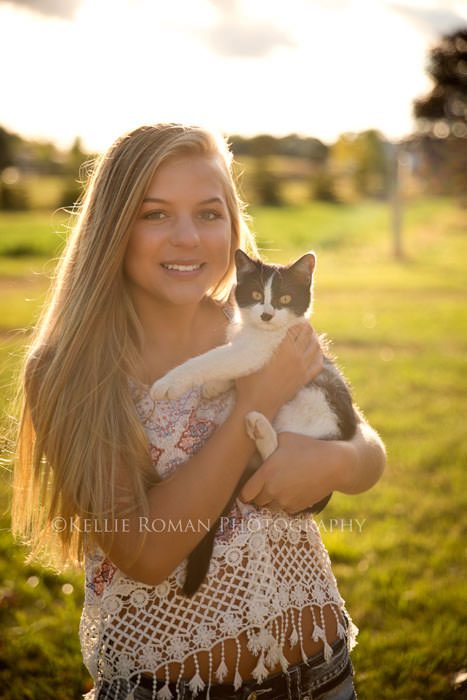 high school senior photos senior girl holding kitting outside in field with sun shining behind them