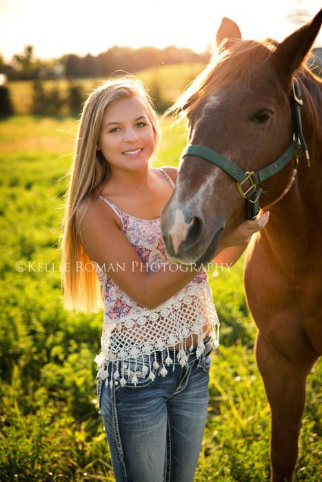 high school senior photos senior girl standing next to horse outside in a field with sun shining through their hair