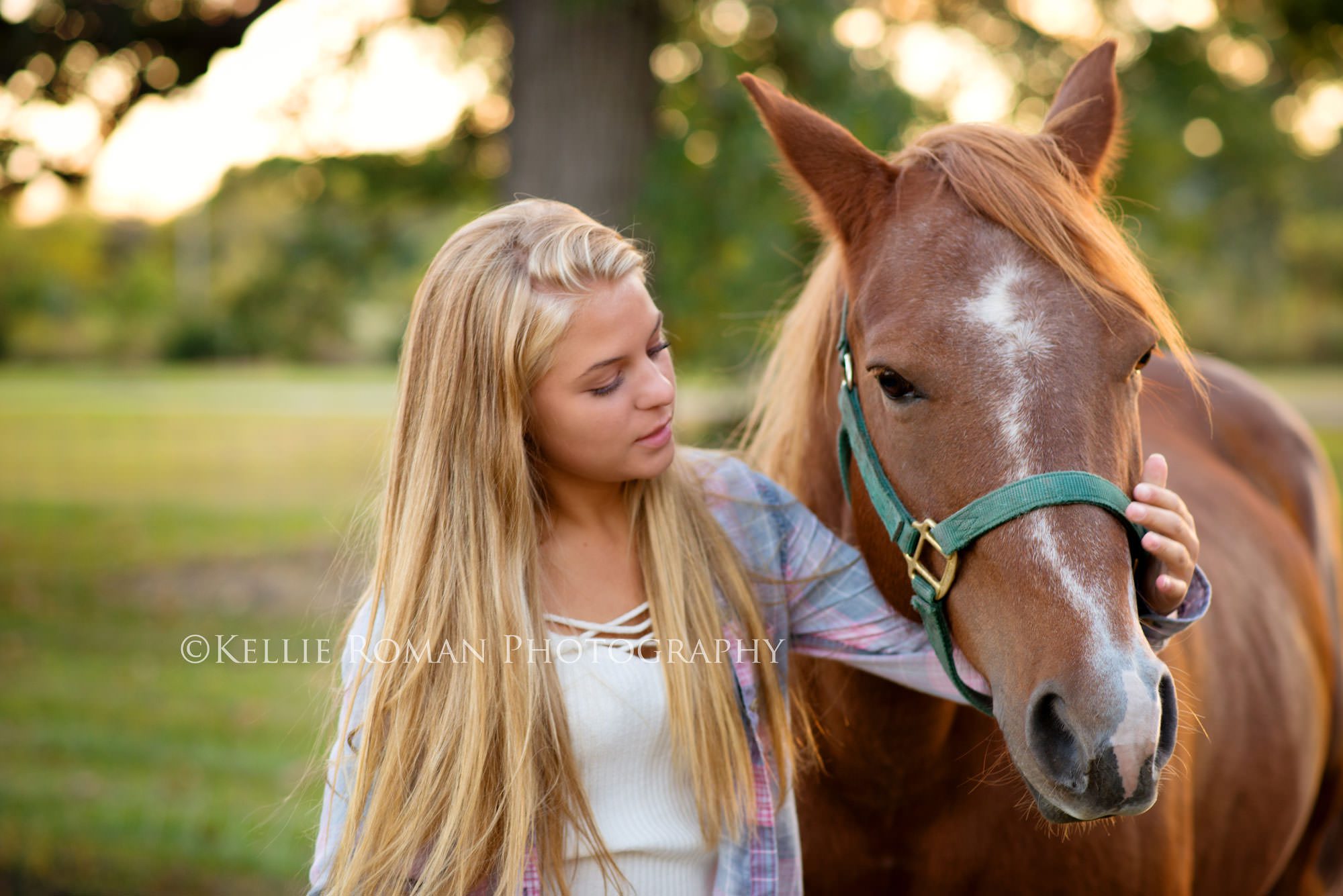 high school senior photos girl standing outside next to a horse. She is looking at the horse with her arm around it's face