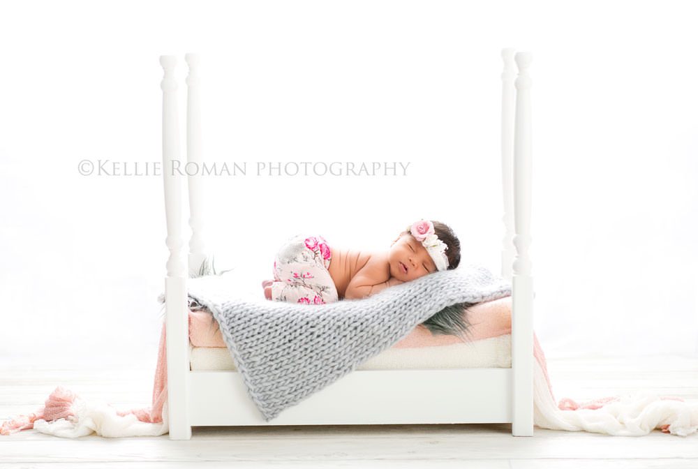 local photographers newborn photography little girl wearing pink and grey pants laying onto of white bed with grey blanket backlighting in studio