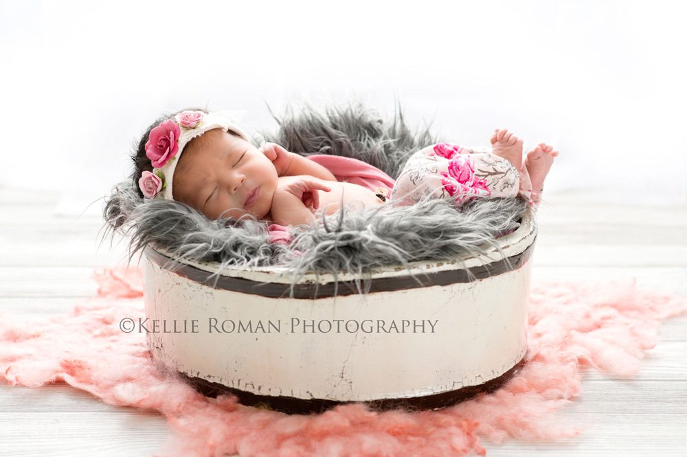 local photographers newborn photographers little girl on back in white bucket onto of pink fur she's wearing pink and grey pants with a pink and white headband on she's sleeping