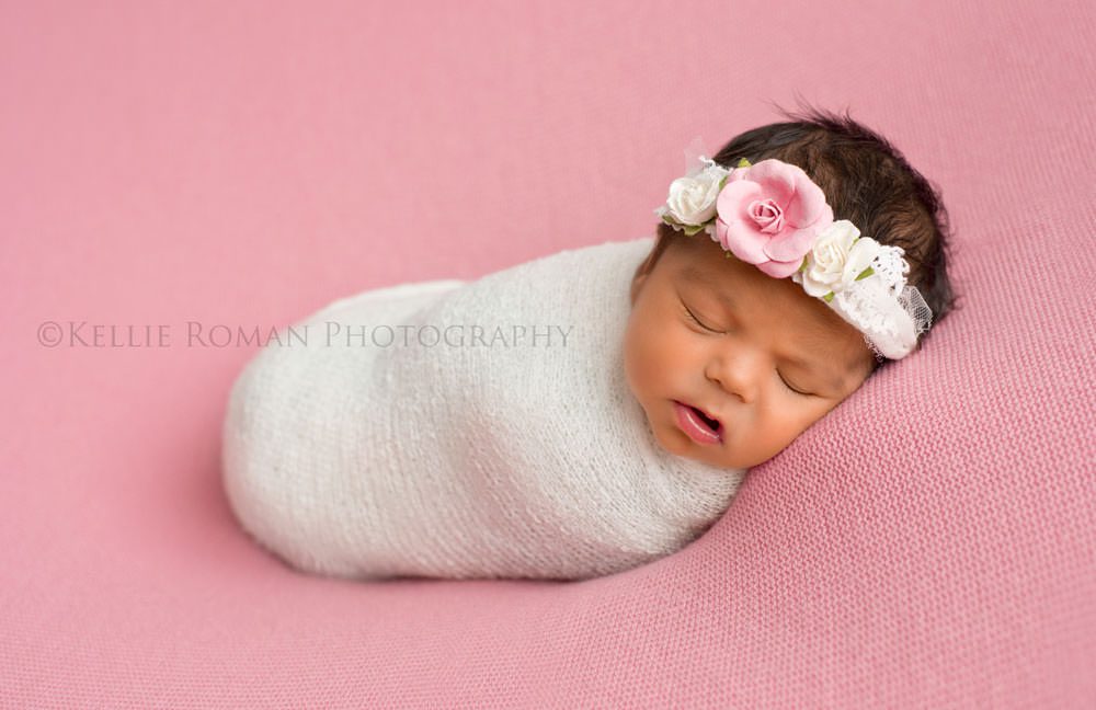 local photographers newborn photographers little girl in a white swaddle wrap onto of a pink blanket sleeping she has on a pink and white headband