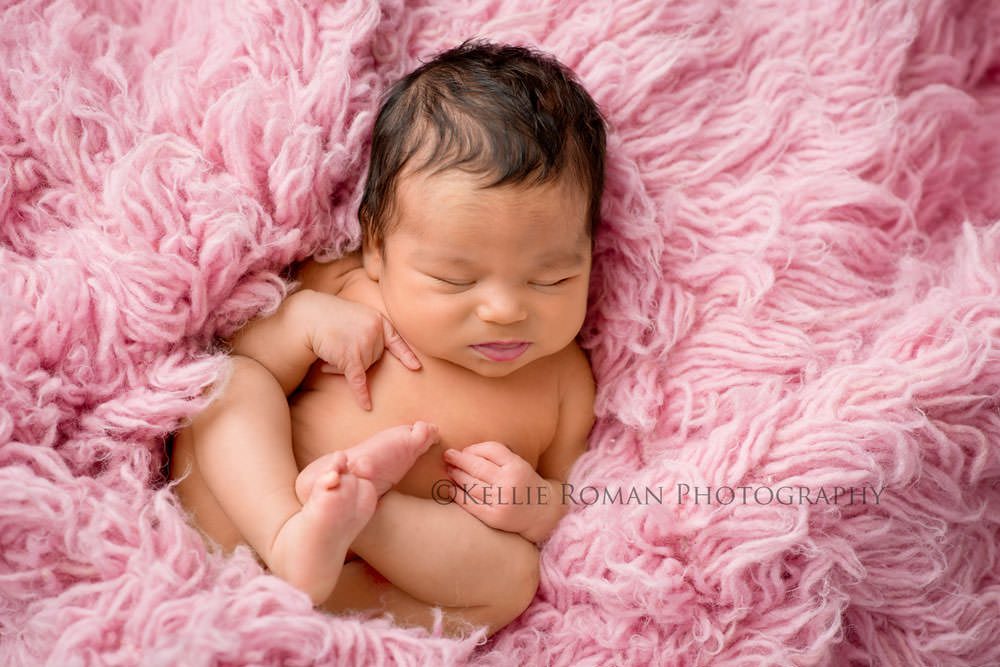 local photographers newborn girl laying curled up on back on top of pink rug sleeping