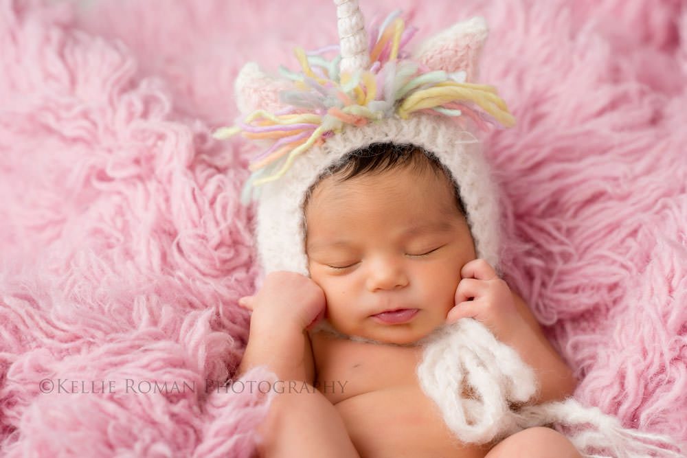 local photographers infant girl laying on back onto of pink rug wearing a unicorn bonnet sleeping