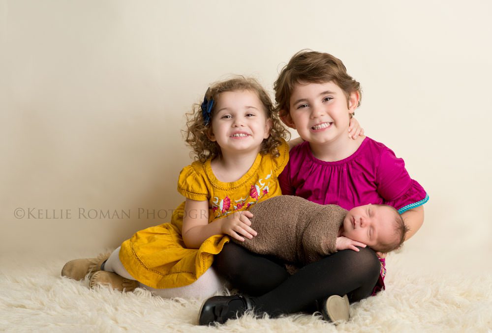 local milwaukee photographers two girls sitting onto of ivory rug wearing fall colors with baby brother sleeping on lap
