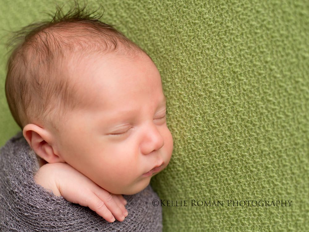 local milwaukee photographers newborn baby boy wrapped in grey swaddle on top of green blanket with hand sticking out of swaddle 