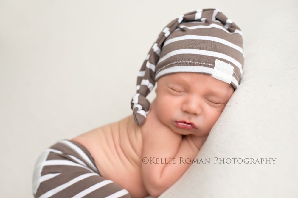 local milwaukee photographers newborn boy with striped hat and pants on sleeping on belly on top of ivory blanket