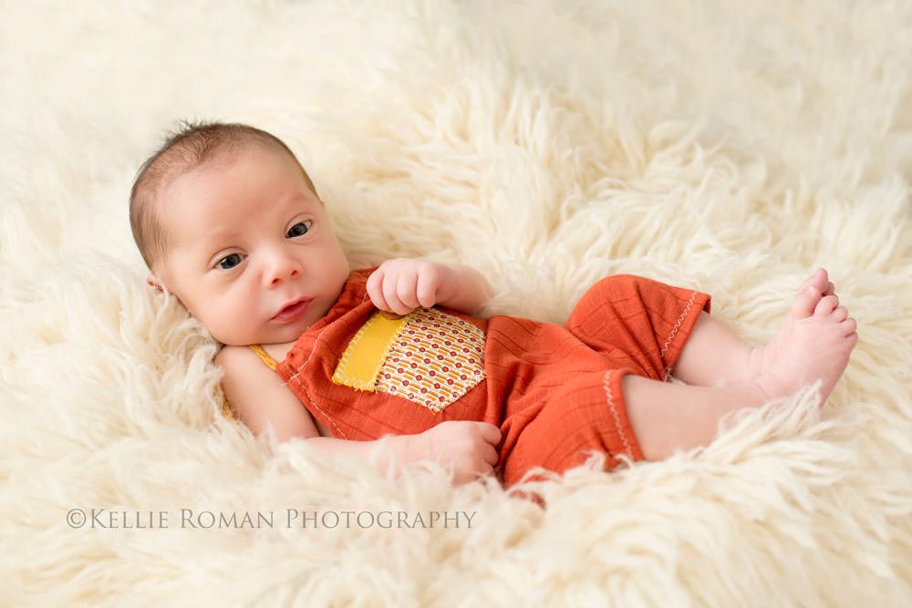 local milwaukee photographers newborn boy in orange and yellow romper laying in ivory rug wide awake looking at camera