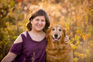 milwaukee senior pics girl sitting in a field with golden fall colors she has a dark plum shirt on and has her golden retriever with her