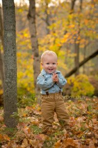milwaukee child photographer boy standing in fall leaves in a park wearing khakis a denim shirt and suspenders