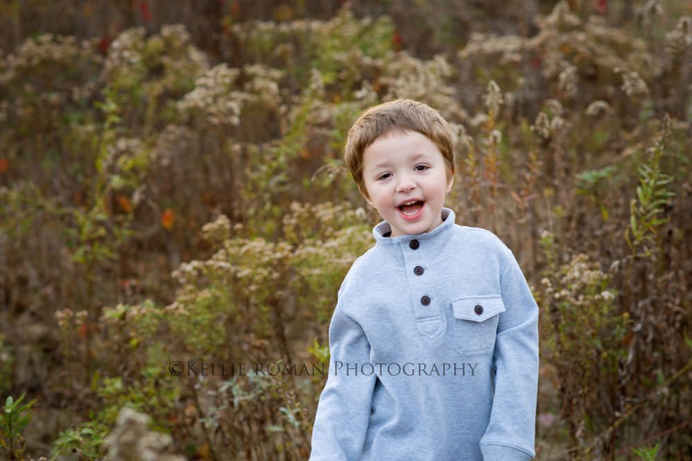 outdoor family photographer boy wearing a grey sweater with buttons outside in a park he is smiling very big at the camera