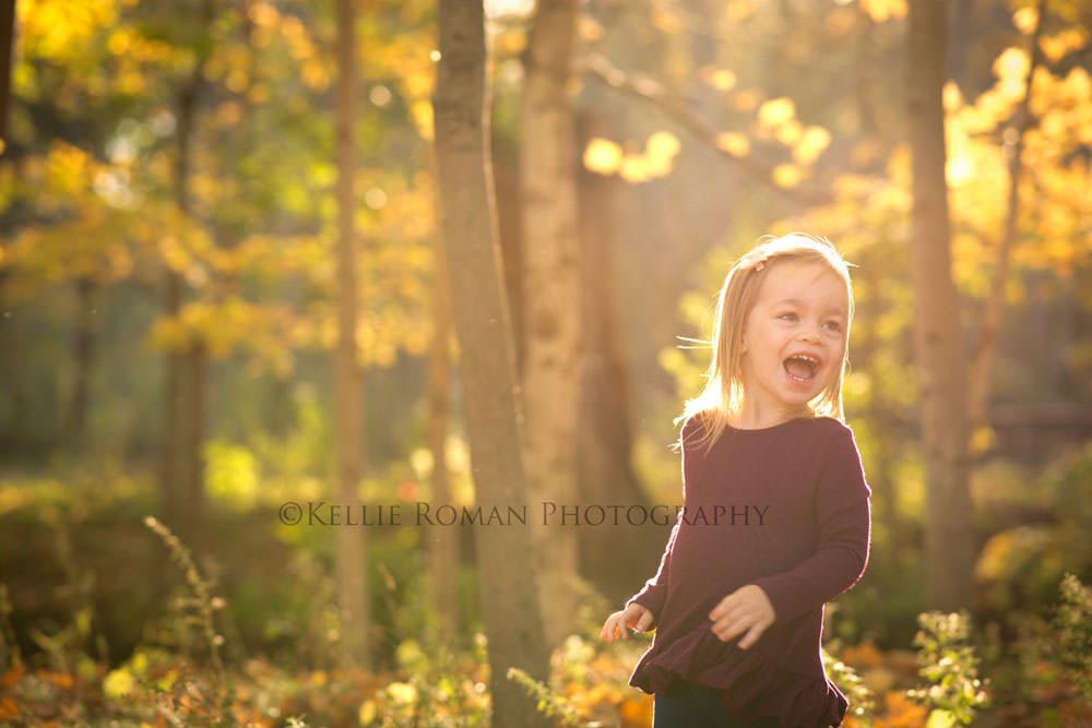 fall sunlight family photographer little girl running and laughing outside at park in the sunshine she's wearing a maroon sweater