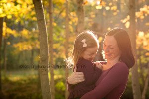 fall sunlight family photographer little girl being held by mother and laughing outside in a park they are both wearing maroon sweaters