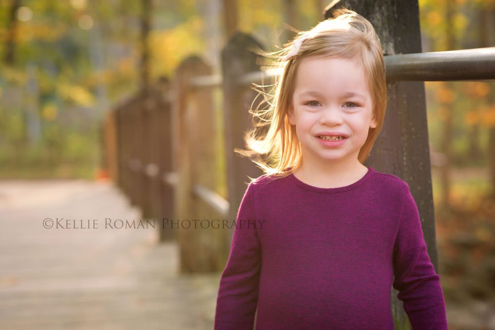 fall sunlight family photographer little girl standing on bridge in the sunlight she's wearing a maroon sweater and the sun is shining through her hair