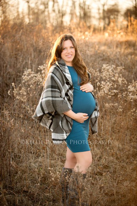 maternity pics in november a women who's pregnant standing in a field of tall brush holding her belly
