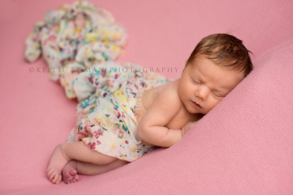 newborn pics milwaukee studio a little newborn girl sleeping on top of a pink blanket posed on her side she has a floral wrap around the middle of her body