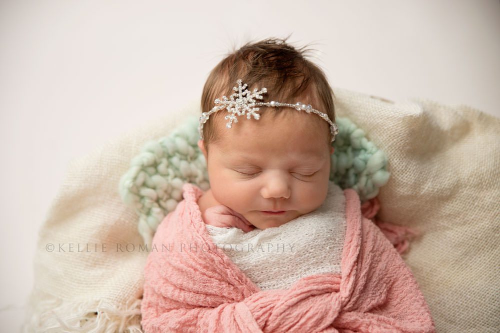 newborn pics milwaukee studio an overhead shot of a newborn girls face she's swaddled in a pink wrap and wearing a crystal bead snowflake shaped headband she has one hand up by her face