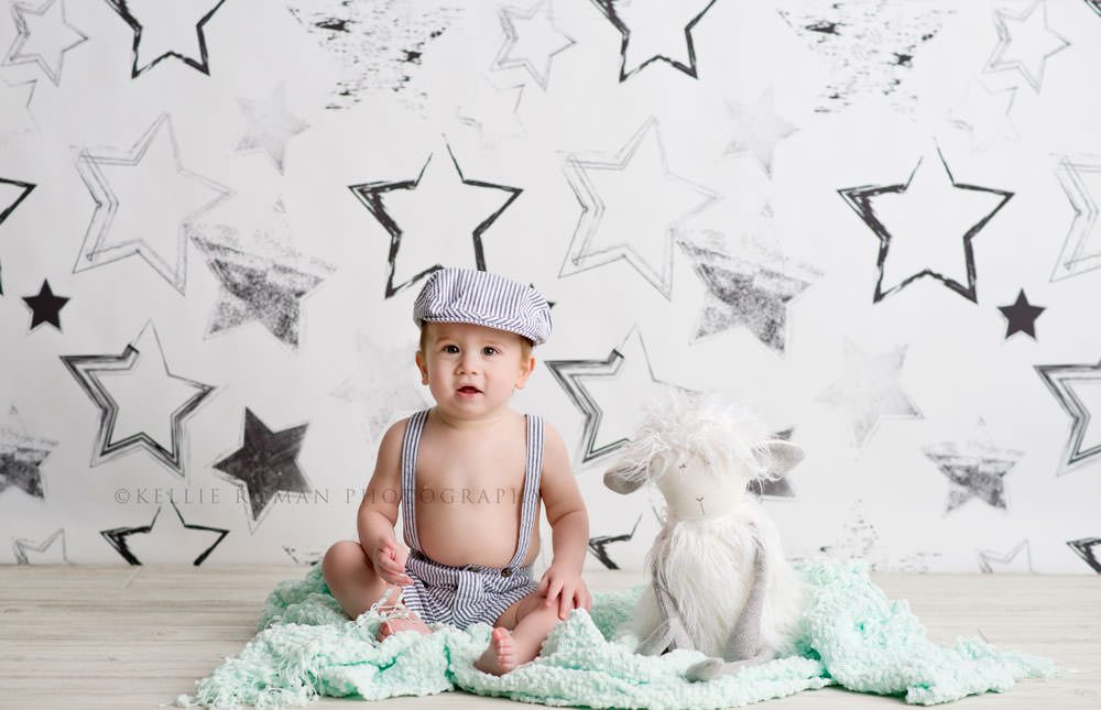 simple cake smash a boy sitting on top of a light teal blanket with a white furry stuffed animal he is in front of a black and white stars backdrop