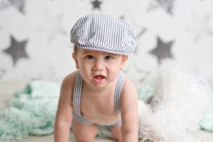 children studio milwaukee photographer simple cake smash a one year old boy with a seersucker romper and hat on looking straight into the camera he is on a teal blanket
