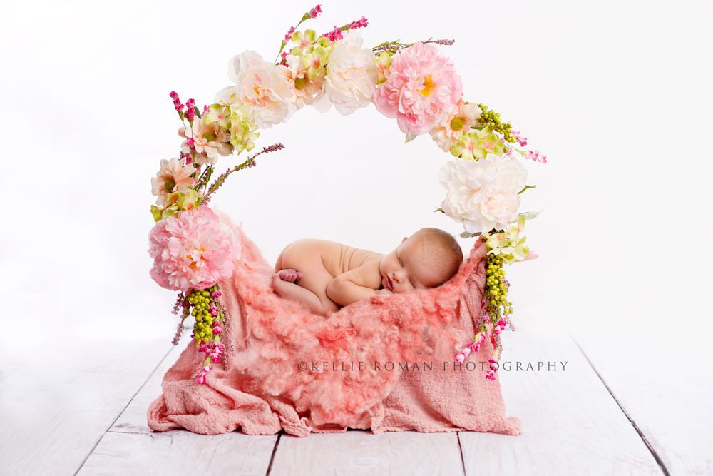 newborn girl in studio a baby girl in milwaukee photo studio naked and posed sleeping on top of a ring with pink and green flowers the image is backlit so its very bright white