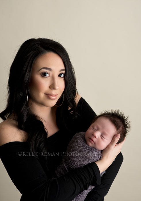 milwaukee newborn pics a family from kenosha having newborn pics in milwaukee studio a mother wearing all black with dark long black hair is smiling at the camera while holding her newborn son the baby is wrapped in a grey cloth